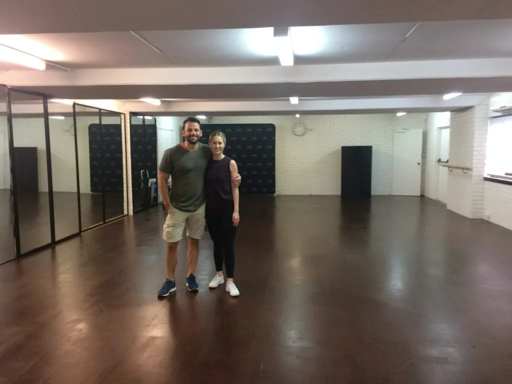 Two people in an empty dance studio with a JuJu clear-finished sprung floor
