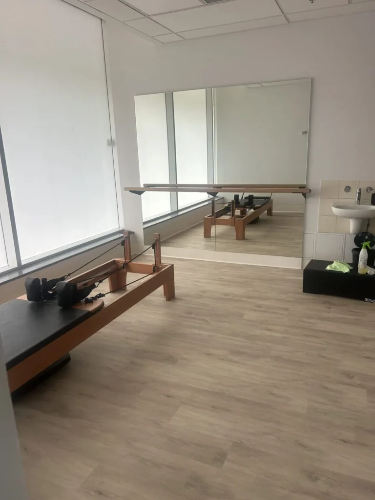 Mirror wall bracket barre and mirror beside a Pilates reformer in a physio studio